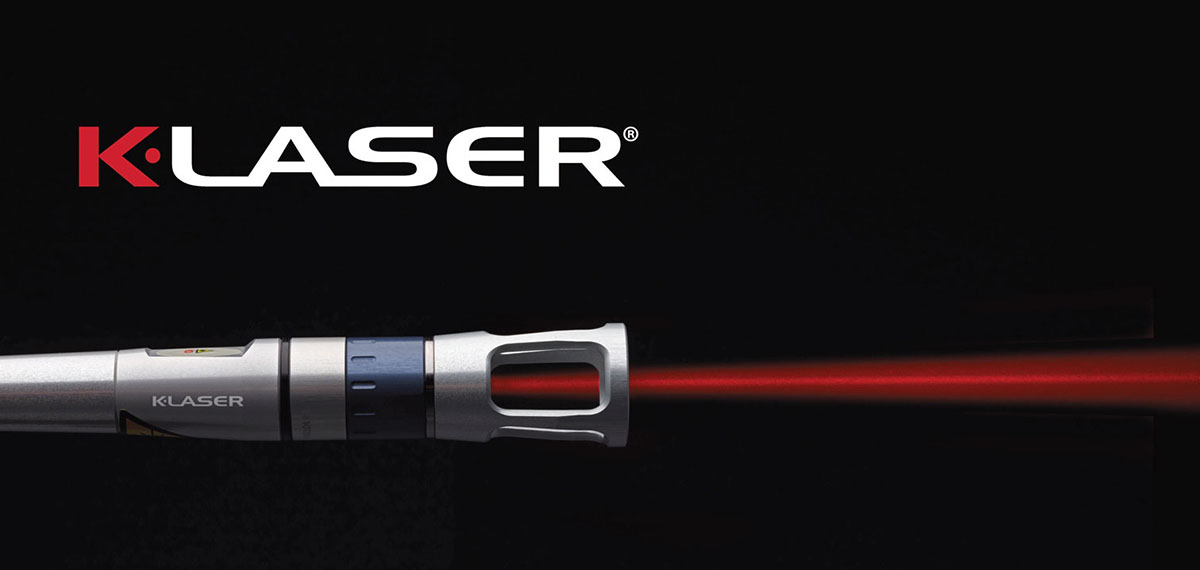 Close-up of a K-Laser device tip projecting a red laser beam over a black background.